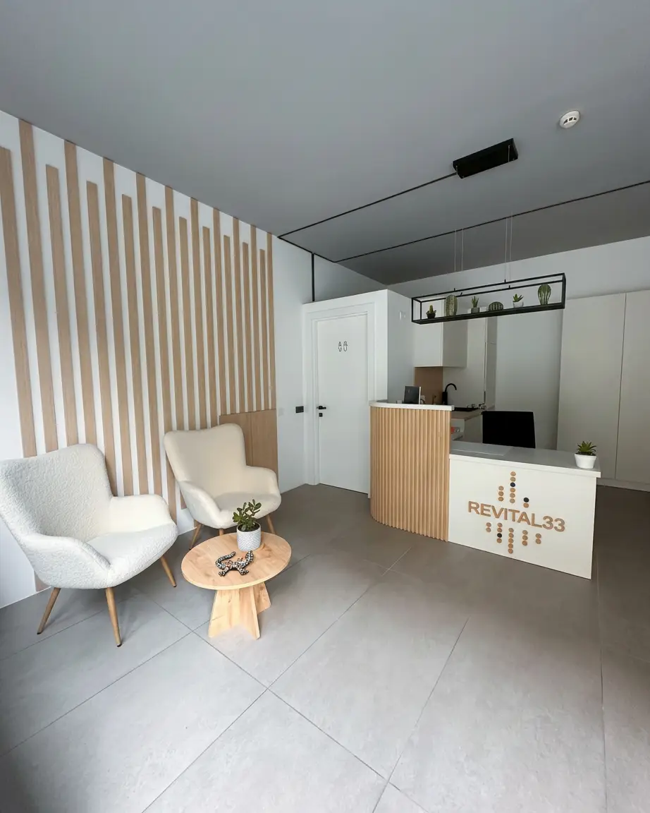 Notranjost recepcije centra Revital33 z dvema belima naslanjačema, leseno mizico in recepcijskim pultom z napisom Revital33.